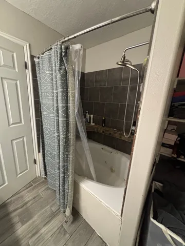 Bathroom featuring a jetted tub, dark tiled surround with decorative accent tile, and a bronzed shower head