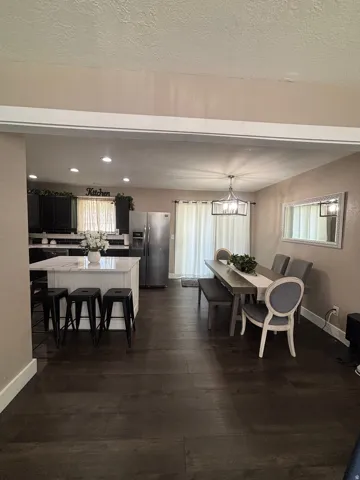 Open-concept kitchen and dining area featuring dark wood-finish flooring, a white kitchen island with a quartz-look countertop, recessed lighting, and a modern dining room chandelier