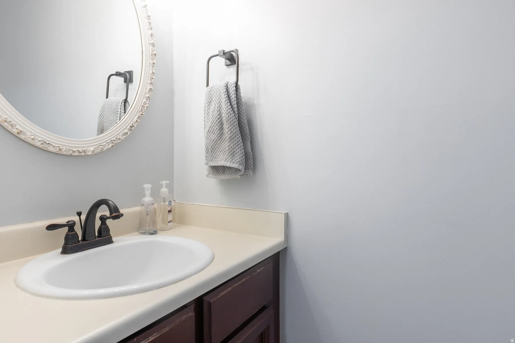 Bathroom vanity featuring an oval undermount sink, oil-rubbed bronze faucet, beige countertop, and dark wood-finish cabinetry