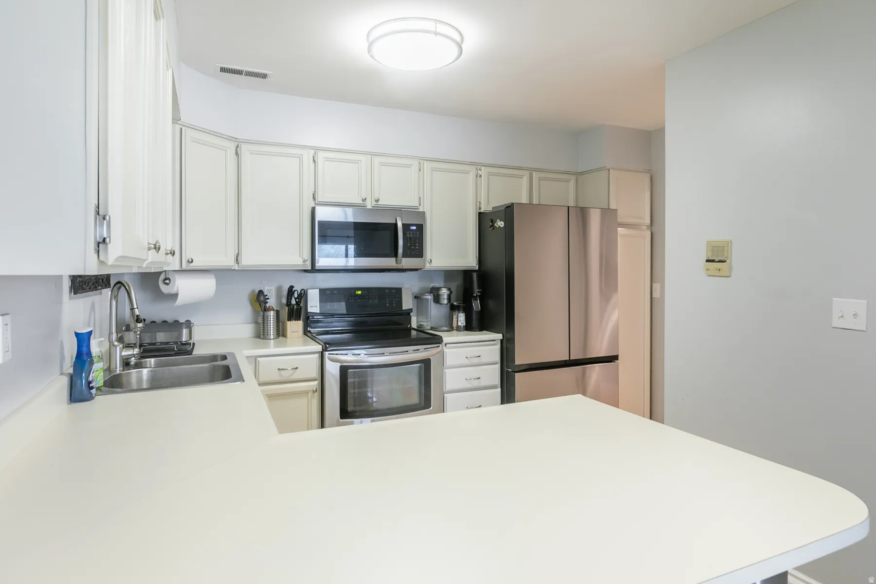 Kitchen featuring white cabinetry with silver hardware, white countertops, stainless steel appliances, and a double basin sink