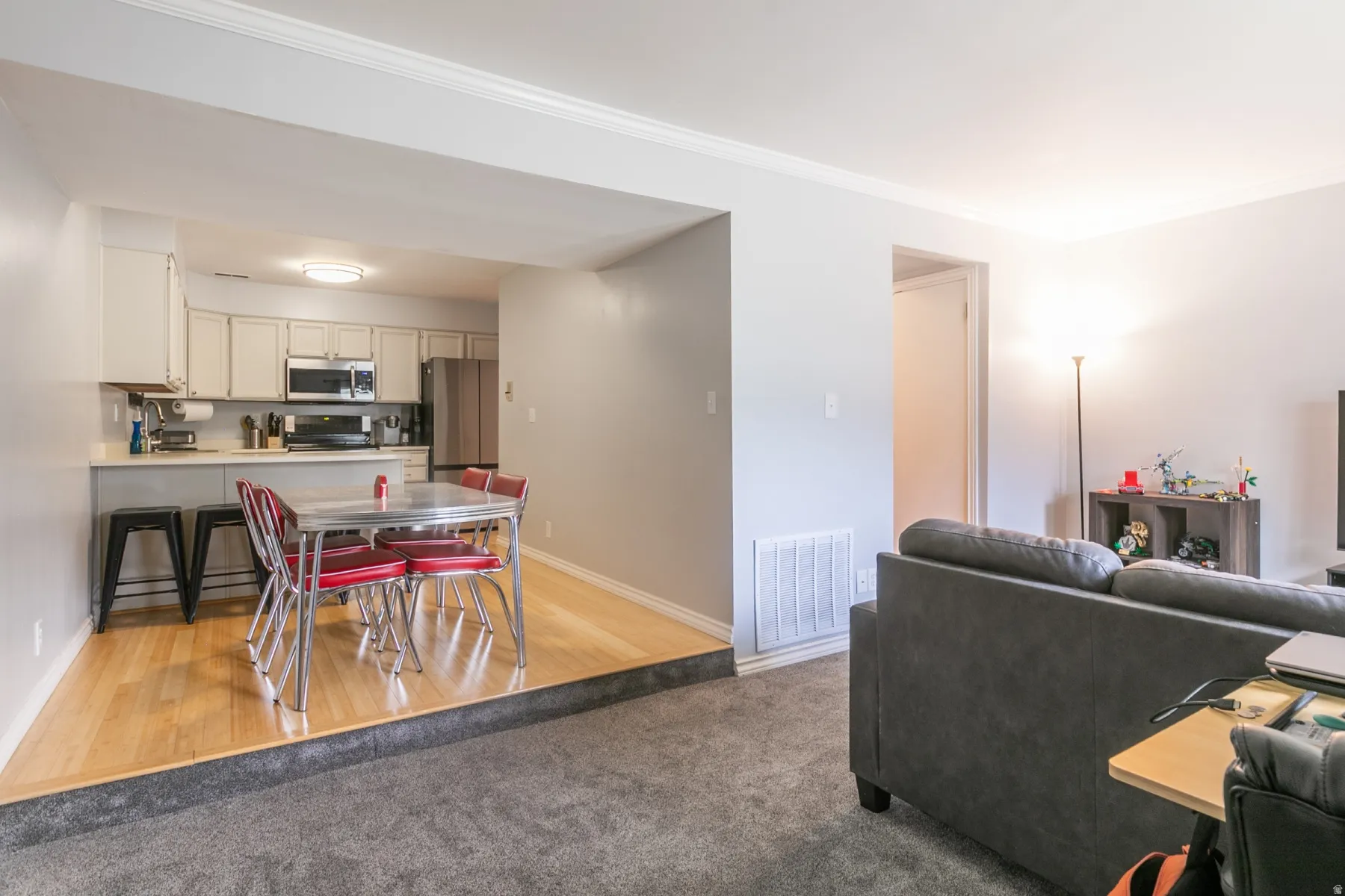 Kitchen and dining area featuring wood-finish flooring, white cabinetry, stainless steel appliances, and a breakfast bar with seating