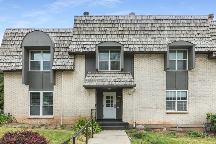 Cream brick exterior featuring a white entry door, black handrail, and gray dormer windows