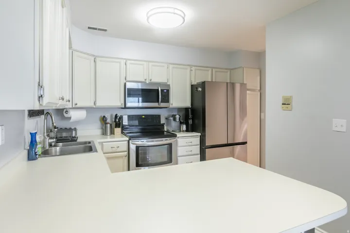 Kitchen featuring white cabinetry with silver hardware, white countertops, stainless steel appliances, and a double basin sink