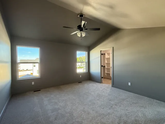 Vaulted ceiling with a ceiling fan, two windows, wall-to-wall carpeting, and a built-in closet with shelving