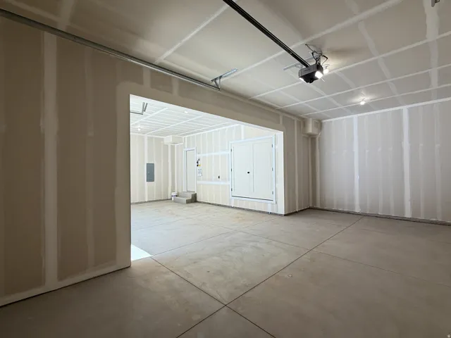 Concrete flooring with exposed drywall, an overhead garage door track, and an automatic garage door opener