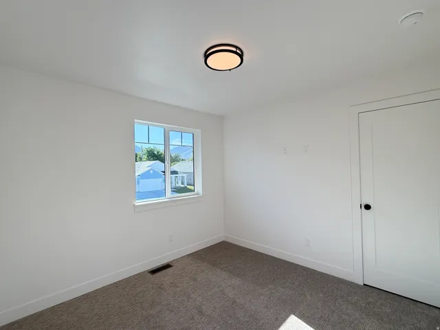 White interior walls, modern flush mount ceiling light, white trim, grey carpeting, and a white interior door with black hardware