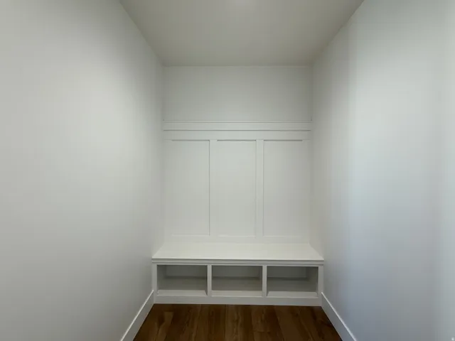 Built-in bench with integrated shelving, wainscoting detailing, and wood-finish flooring