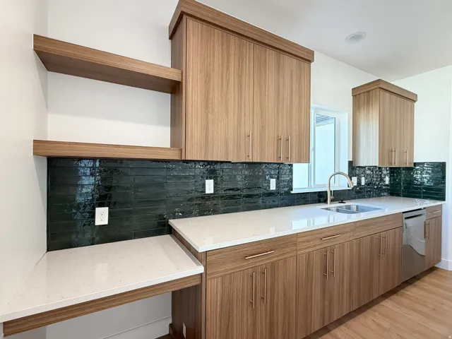 Wood-finish cabinetry, dark subway tile backsplash, light-toned countertops, stainless steel sink, and wood-finish flooring