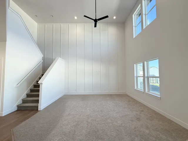 High ceilings with recessed lighting, shiplap accent wall, staircase with carpeted treads, wood-finish flooring, and multiple windows