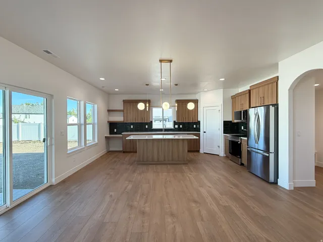 Open-concept kitchen and living area featuring wood-finish flooring, stainless steel appliances, a center island with countertop seating, and a sliding glass door to the exterior
