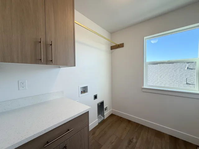Laundry area featuring wood-finish flooring, white quartz-finish countertop, wood-finish cabinetry, and a single window