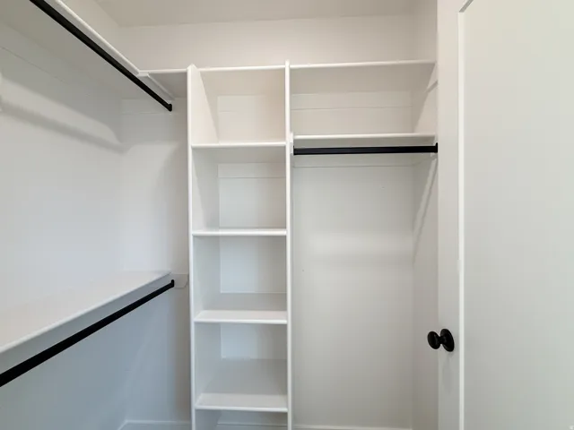 White built-in shelving, white storage shelving, black hanging rods, white walls, and a white door with a black knob