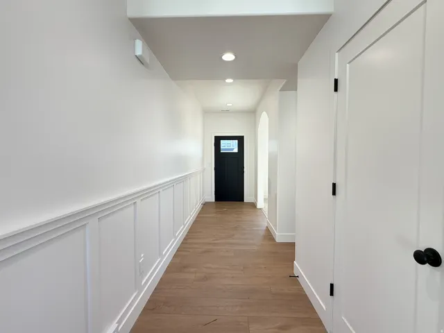 Elegant hallway showcasing crisp white wainscoting, recessed ceiling lighting, and warm wood-finish flooring throughout