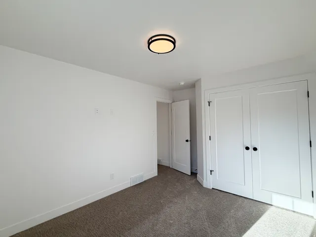 Neutral white walls, flush-mount ceiling light, white paneled bifold doors with matte black hardware, white paneled interior door, and textured carpeting