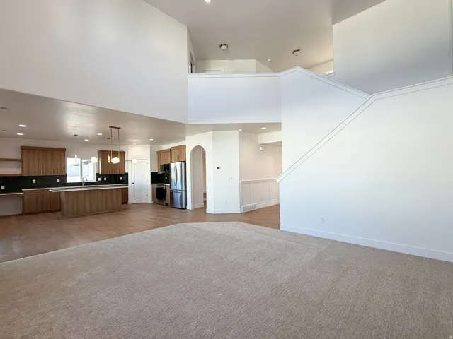 Open-concept living area with high ceilings, a contemporary kitchen featuring wood-finish cabinetry, a large kitchen island with pendant lighting, and an arched doorway