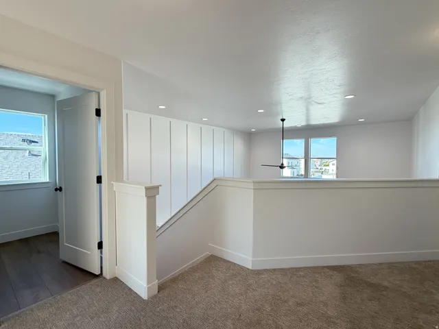 Bright upper-level landing featuring crisp white shiplap wall paneling, neutral carpet flooring, recessed lighting, and dual windows flooding the space with natural light