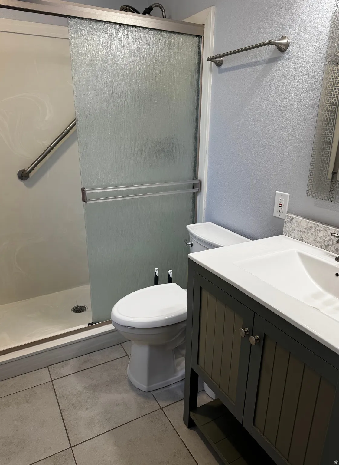 Bathroom featuring a sliding glass shower door, a vanity with an integrated sink, a stone-finish countertop, and large format floor tiles