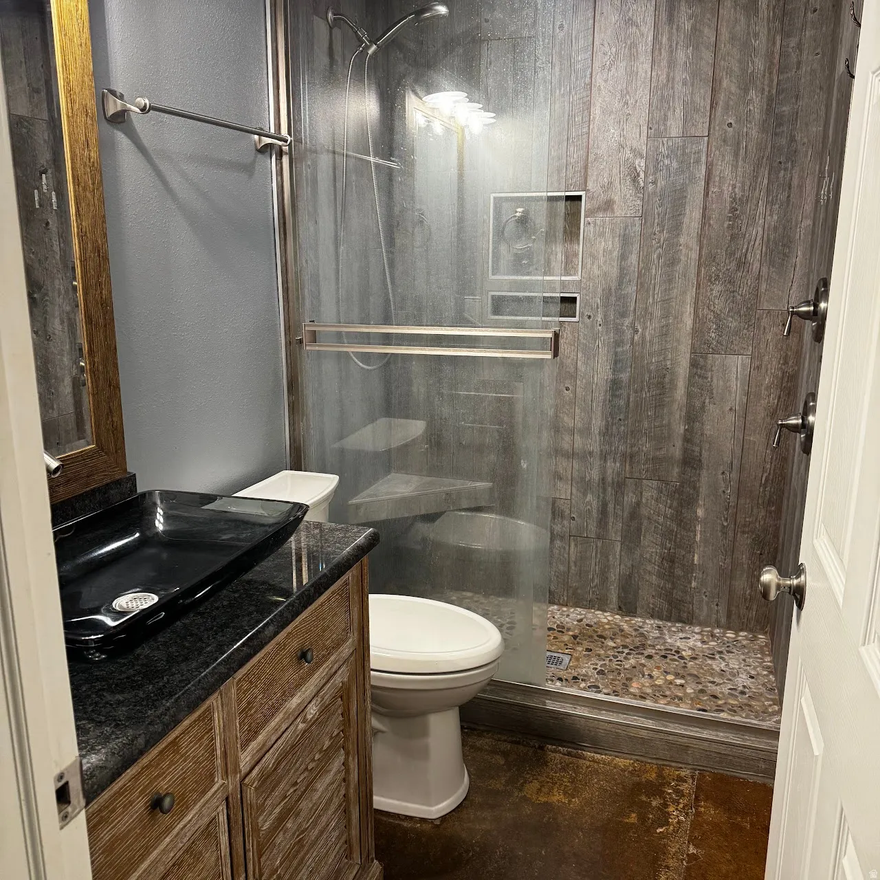 Bathroom featuring a glass-enclosed shower with wood-finish wall panels and a pebble-stone floor