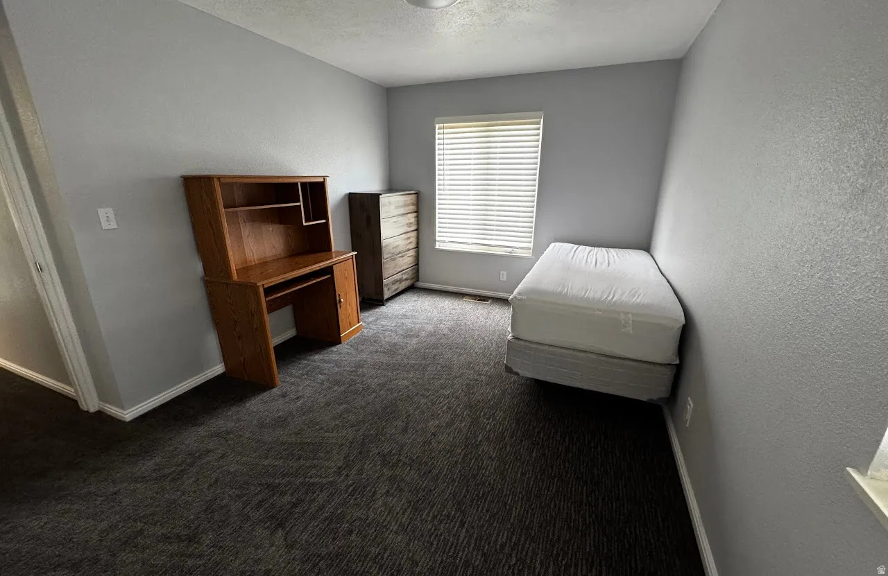Spacious room featuring neutral gray walls, textured carpeting, and a window with horizontal blinds