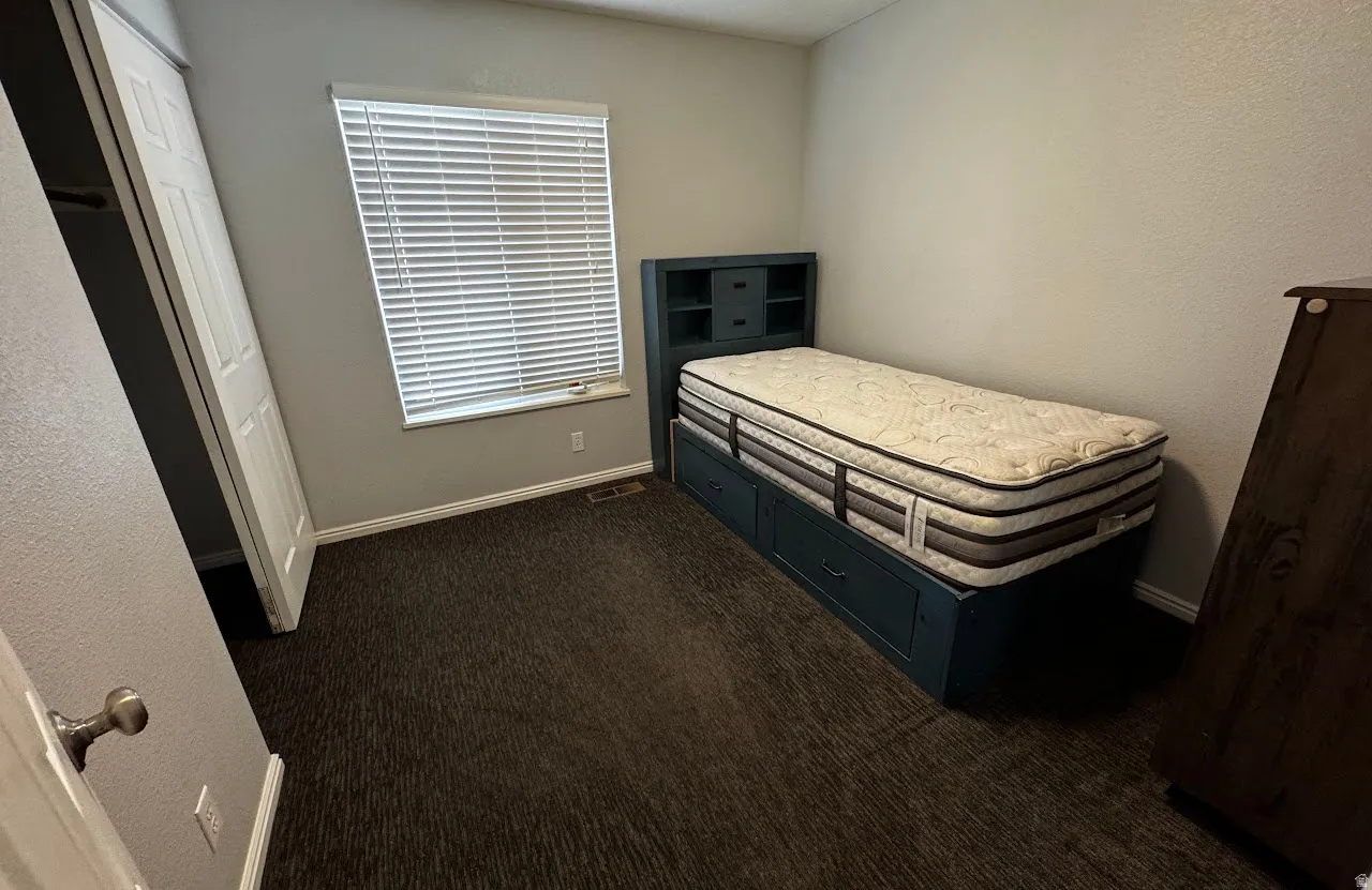 Carpeted interior with a window featuring horizontal blinds, a white door, and white baseboards