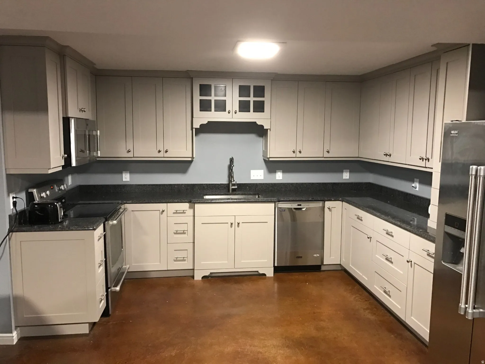 U-shaped kitchen featuring light-toned cabinetry, dark speckled countertops, and stainless steel appliances