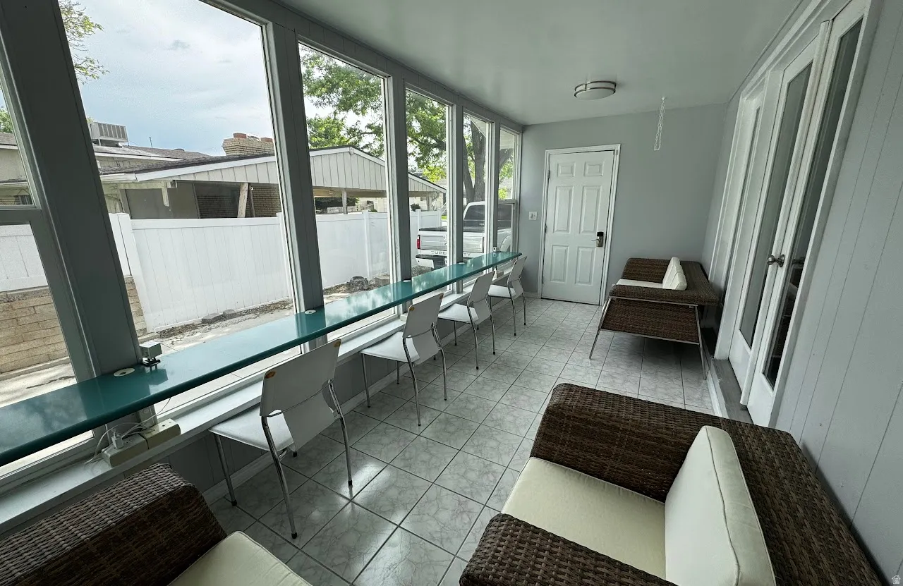 Enclosed sunroom of floor-to-ceiling windows  featuring built-in desk that spans the entire room. The desk features several countertop outlets.