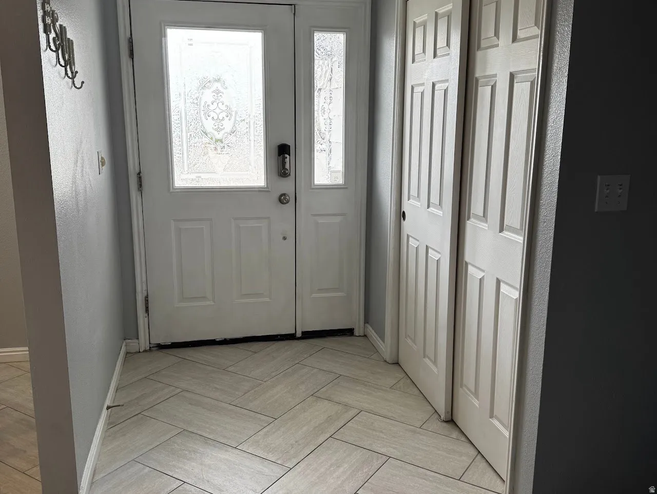 Entryway featuring a decorative frosted glass front door with a digital lock, light gray herringbone tile flooring, and bi-fold closet doors