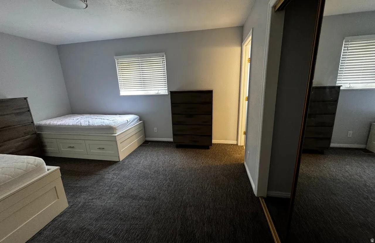 Carpeted room featuring light gray walls, a window with horizontal blinds, and a built-in closet with sliding mirrored doors