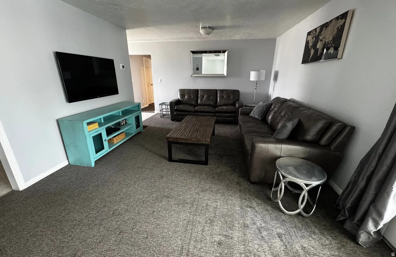 Spacious living area featuring light gray wall paint, newly installed gray high-traffic carpeting, and white baseboards