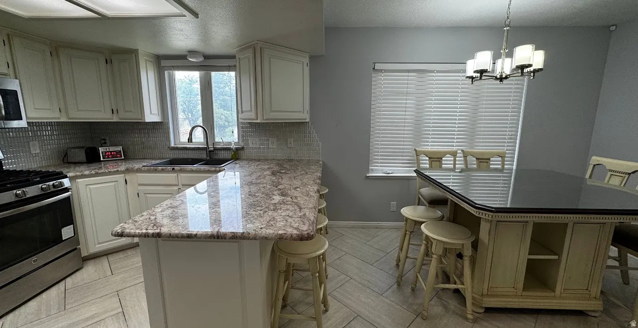 Kitchen featuring solid granite countertops, full cabinetry, stainless steel range, gray herringbone tile floors, white tile backsplash, and spacious seating.