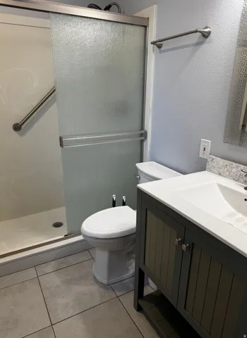Bathroom featuring a sliding glass shower door, a vanity with an integrated sink, a stone-finish countertop, and large format floor tiles