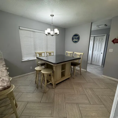 Dining area featuring a central island with a dark countertop, an overhead chandelier with frosted glass shades, and patterned tile flooring