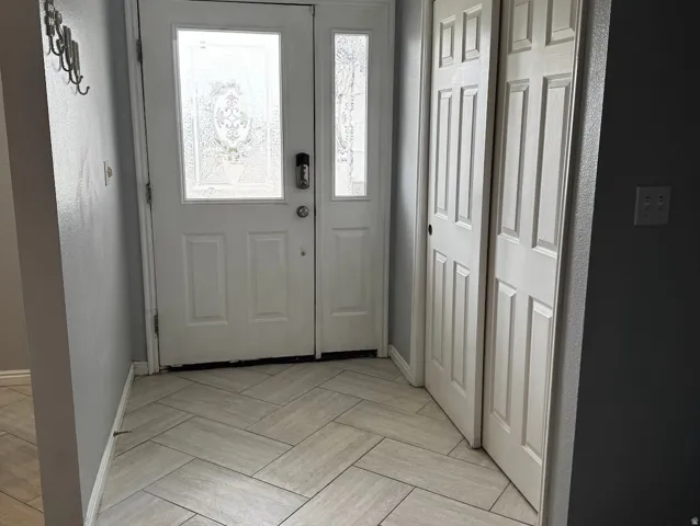 Entryway featuring a decorative frosted glass front door with a digital lock, light gray herringbone tile flooring, and bi-fold closet doors