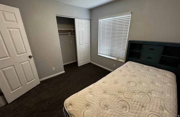 Bedroom featuring neutral gray walls, dark textured carpeting, and white baseboards