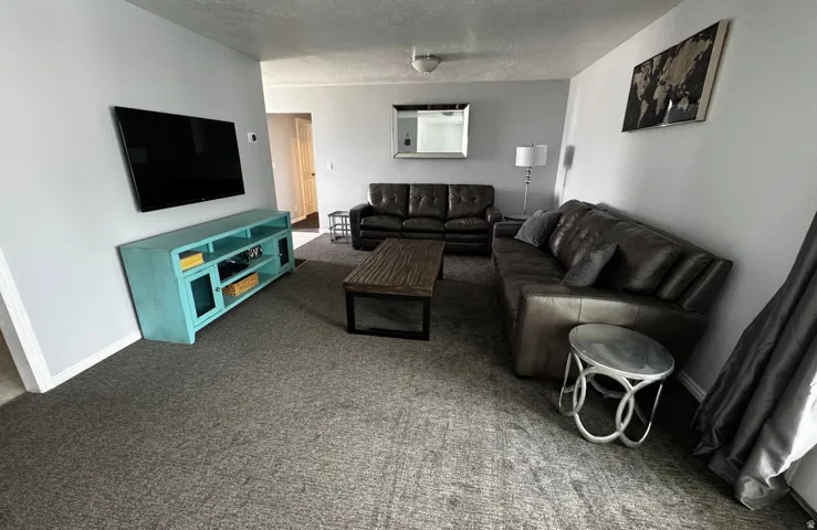 Spacious living area featuring light gray wall paint, newly installed gray high-traffic carpeting, and white baseboards