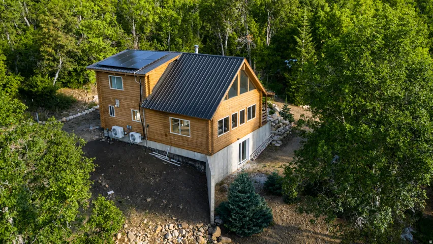 Wood-sided dwelling featuring a dark metal roof, multiple solar panels, and a concrete foundation