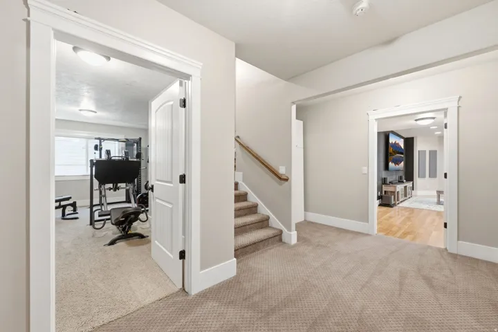Carpeted hallway featuring a staircase with wood railing, leading to two distinct rooms