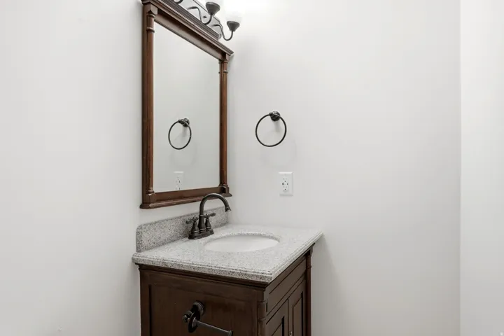 Dark wood-finish vanity with a light speckled countertop, undermount sink, and dark bronze faucet
