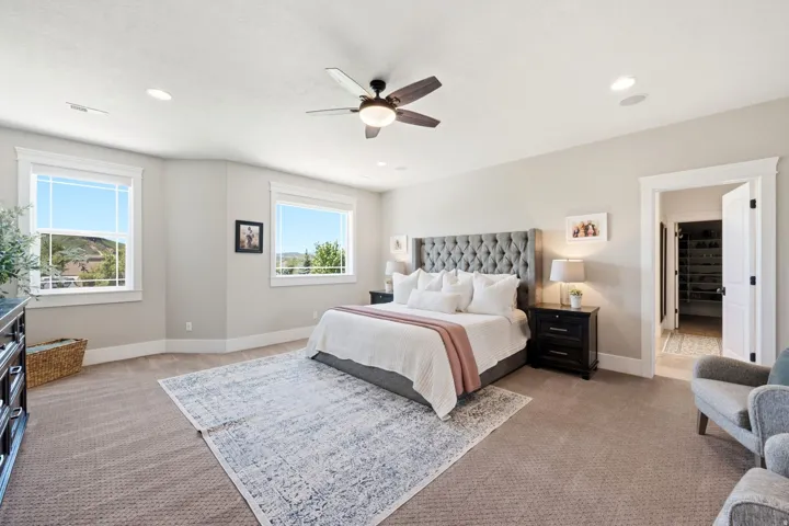 Spacious bedroom featuring neutral carpeting, a ceiling fan, recessed lighting, and two large windows with white trim