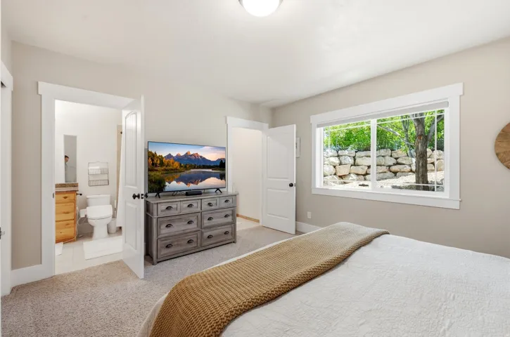 Carpeted bedroom featuring a large window with white trim, a solid white door, and an entryway to an attached bathroom