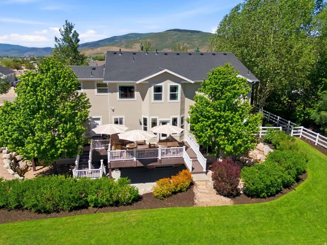 Rear exterior featuring a multi-level deck with white railings, a lower-level patio, and extensive landscaping