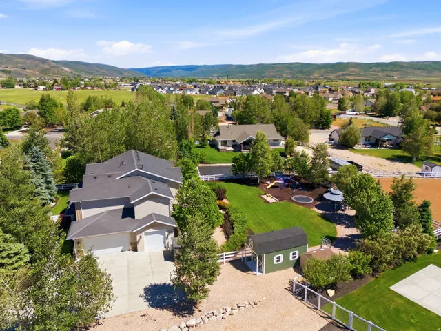 Spacious property featuring a large residence with an attached garage, expansive green lawn, mature trees, and a detached green shed