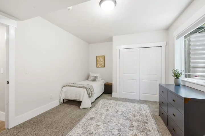 Carpeted room featuring a window with a window blind, a ceiling-mounted light fixture, white trim, and a double-door closet with arch paneling