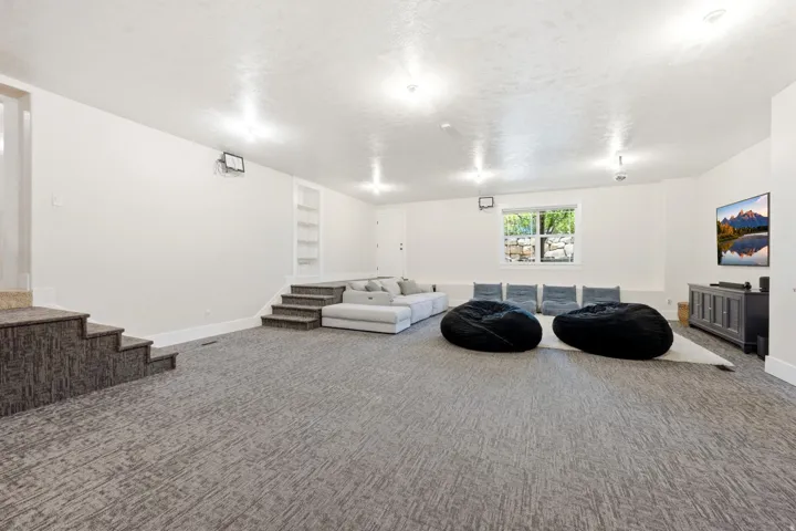 Lower-level entertainment space featuring textured carpeting, recessed lighting, and a built-in shelving unit