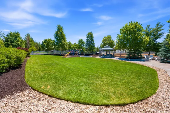 Expansive lawn area featuring a paved pathway, a built-in gazebo, mature trees, and a white perimeter fence