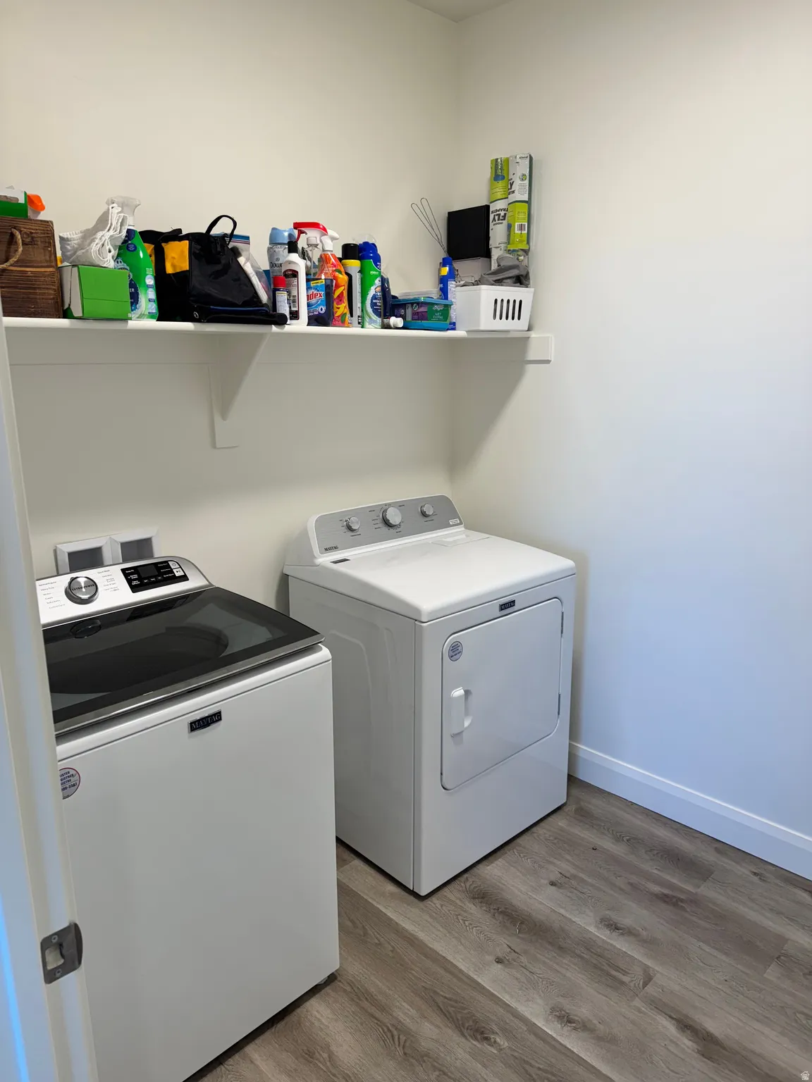 Laundry area featuring wood-finish flooring and a wall-mounted storage shelf