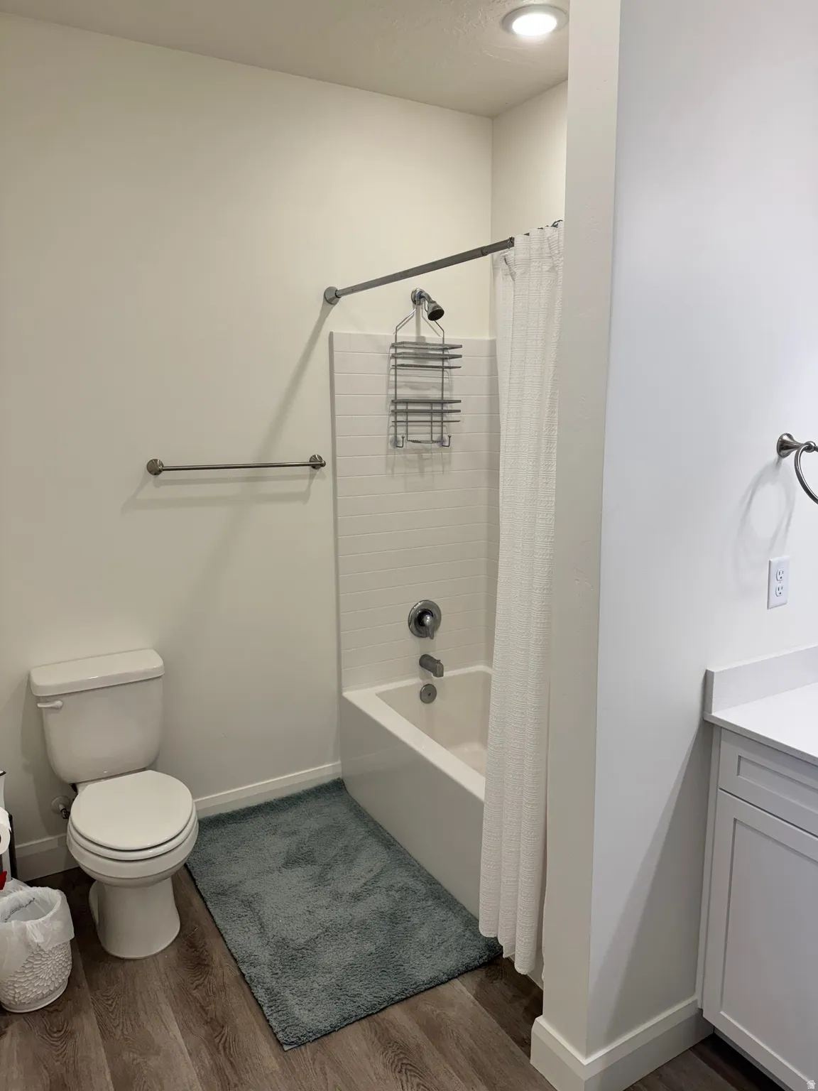 Bathroom featuring a white tub/shower combination with subway tile surround, a toilet, and wood-finish flooring