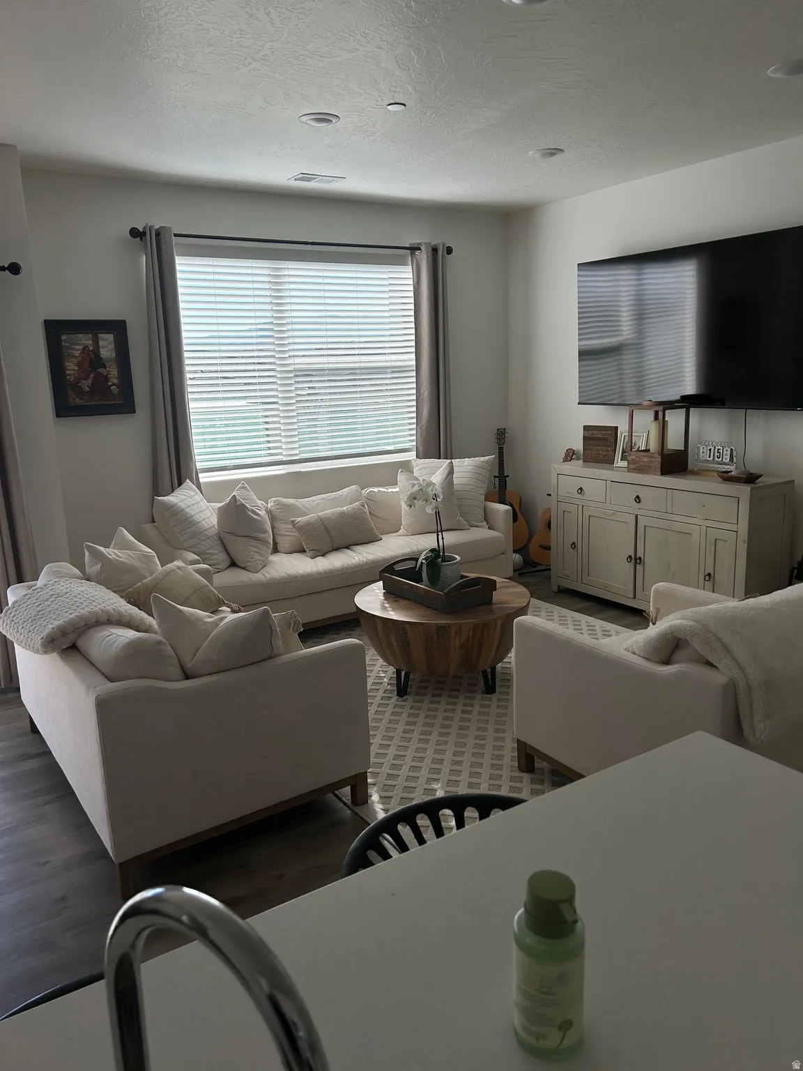 Spacious living area featuring a large window with blinds and drapes, recessed lighting, and wood-finish flooring