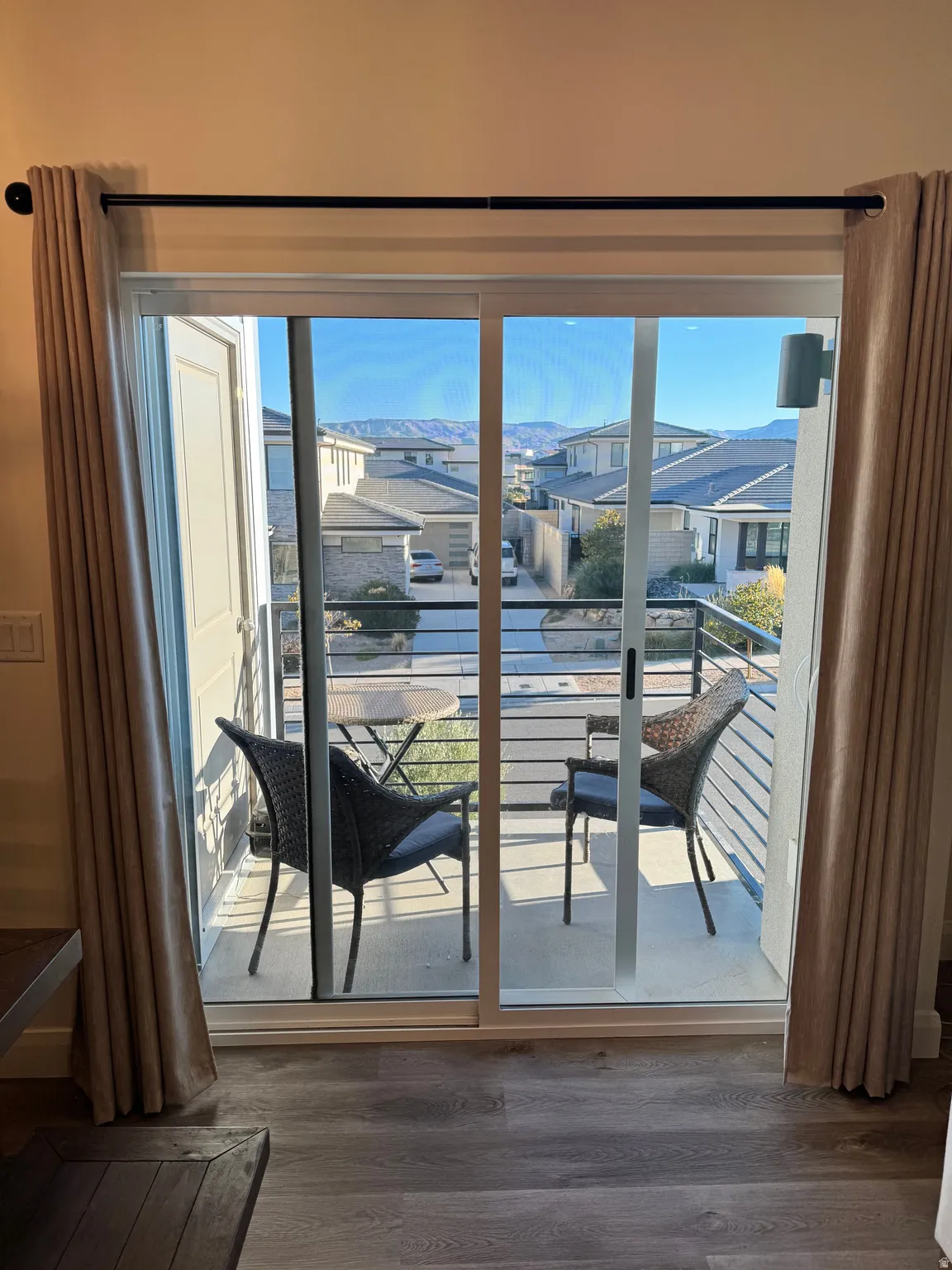 Sliding glass door opening to a private balcony with horizontal metal railings, showcasing distant hills