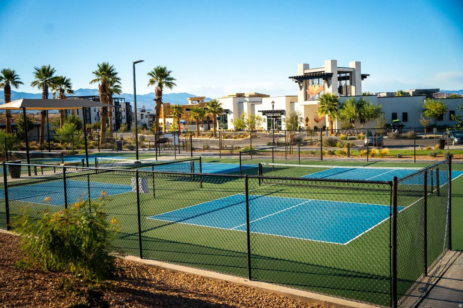Multiple pickleball courts featuring blue and green playing surfaces, surrounded by black chain-link fencing